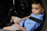 A teenage boy wearing seat belts travels by car in a protective child booster car seat. Traveling safely with children.