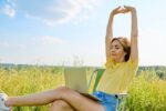 Adult woman sitting on an folding camping chair using a laptop, in a meadow with wild herbs