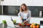 Happy young woman making a salad at the kitchen