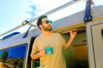 man in charming trailer house makes coffee outdoors in mountains in summer sunny day