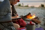 Charming young woman writing in notebook while resting near campfire