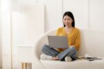 Pretty young korean woman sitting on couch, using laptop
