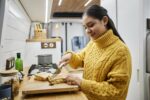 Smiling young woman making breakfast travelling in trailer van