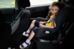 Baby girl belted in a safety child car seat, smiles while looking at the camera. Using a child car seat to travel safely with children in a car