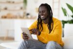 Technologies For Leisure. Black Happy Man Using Digital Tablet At Home