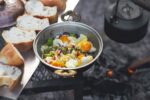 Detail view of camp fire cooking, breads are in a row, a tea pot and egg pan is on the fire with copy space