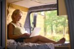 Senior Woman On Camping Trip In Countryside Working Inside RV Using Laptop